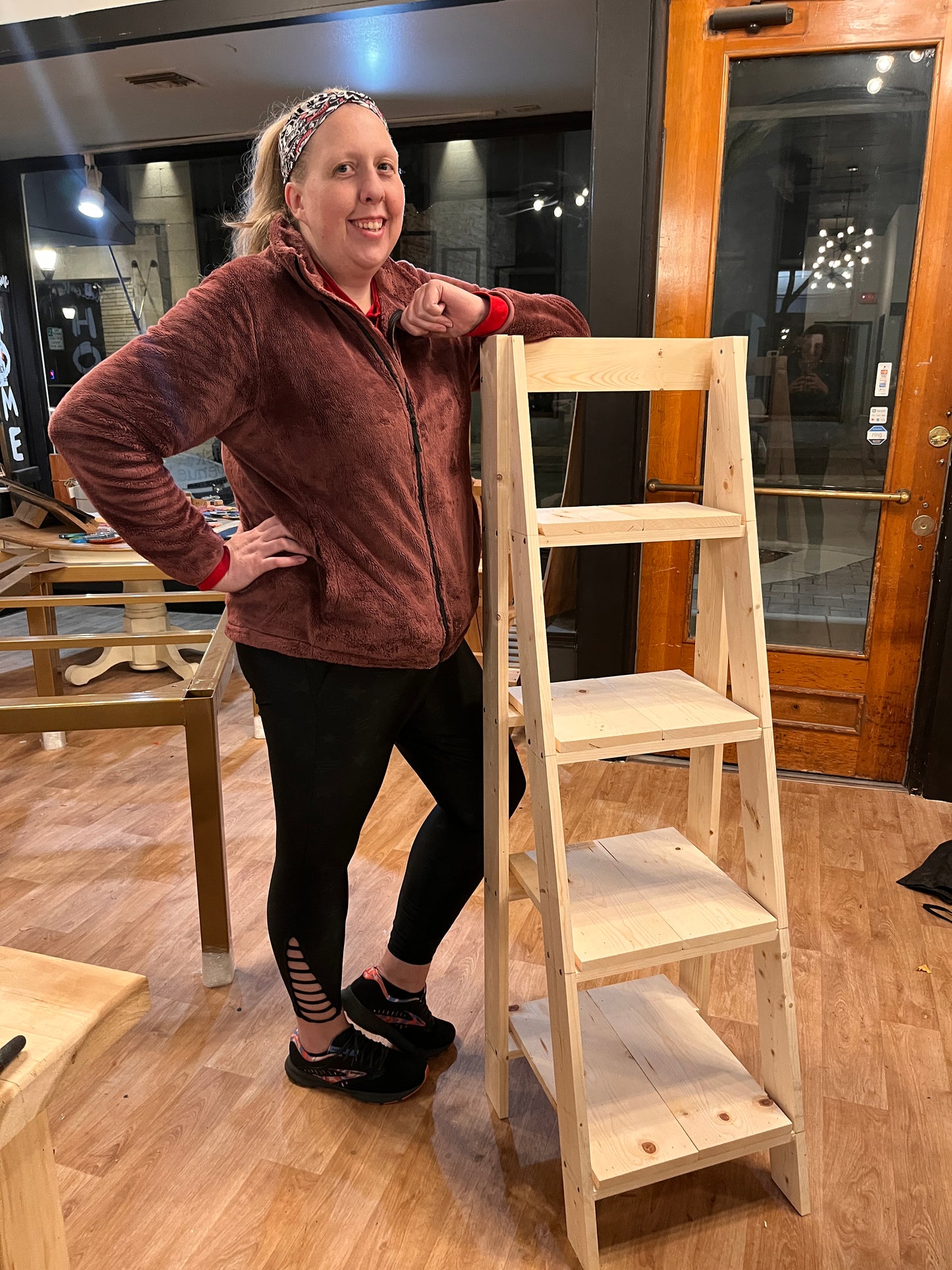 Person leaning on a wooden shelf in a room with wooden flooring and furniture.
