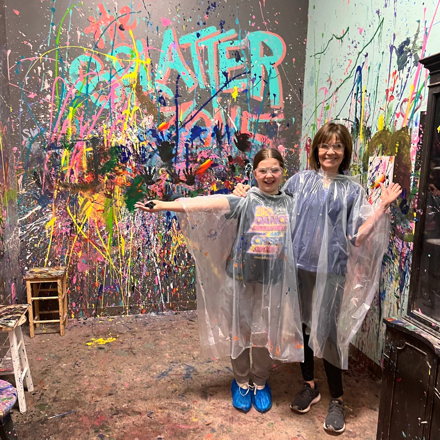 Two people standing in front of a colorful splatter-painted wall.