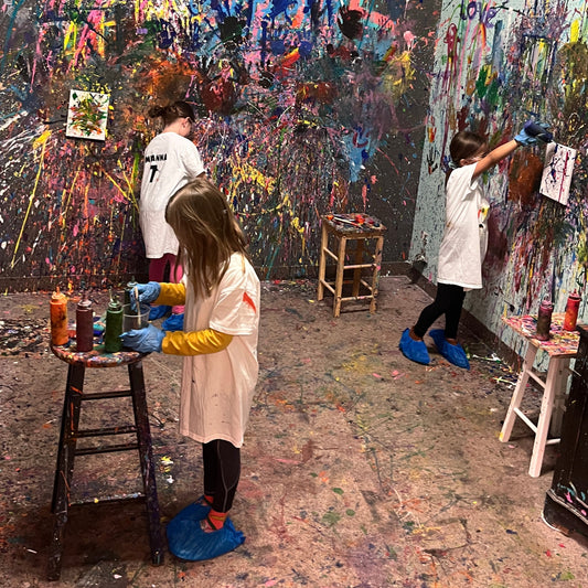 Four children in a splatter room with colorful painted art on the walls and floor.