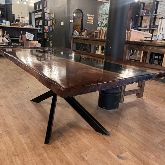 Corner view of a wooden epoxy river dining table with black metal legs on a wooden floor.
