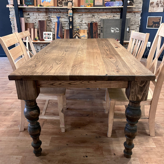 Wooden dining table with chairs and turned legs in a room with a wooden floor and stone walls.
