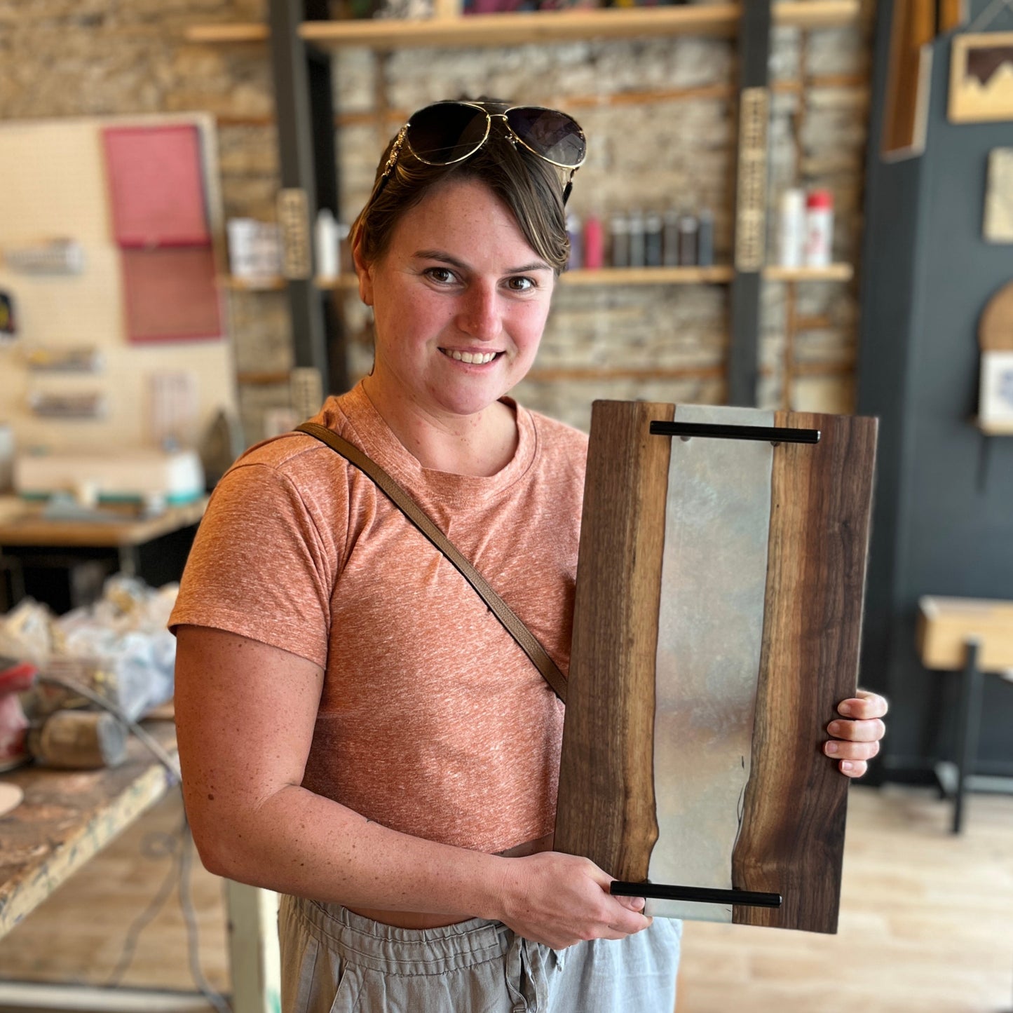 Person holding an epoxy river serving tray with live edge wood in a workshop setting