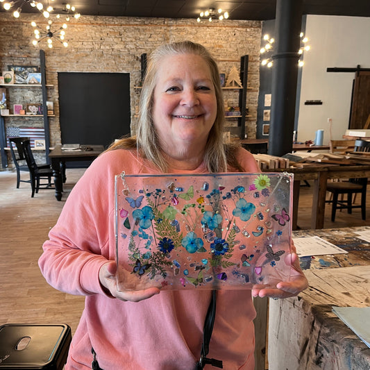 Person holding a colorful epoxy sun catcher with pressed flowers and butterflies in a studio workshop