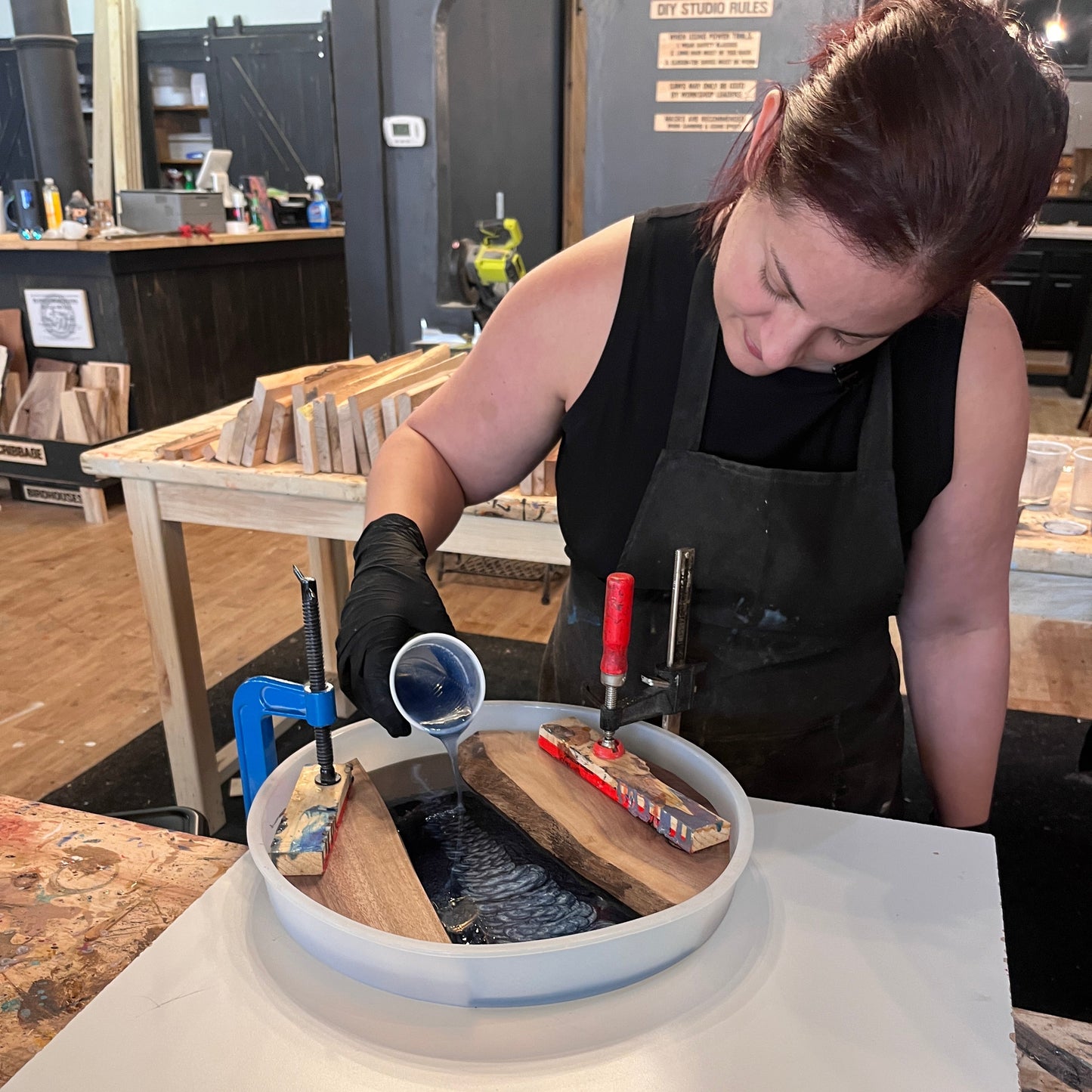 Person working on a round epoxy river serving tray project with tools and materials in a workshop setting