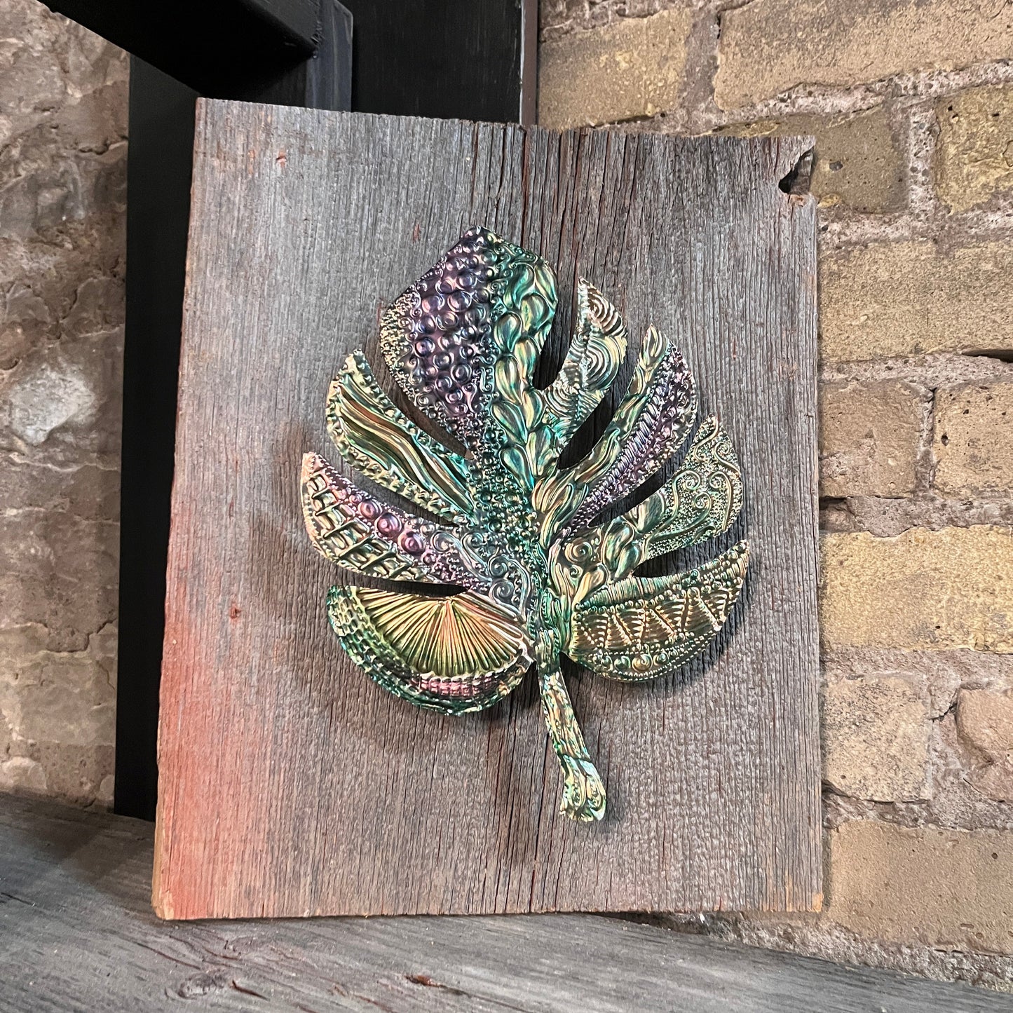 Decorative copper leaf sculpture on a wooden board against a stone wall background