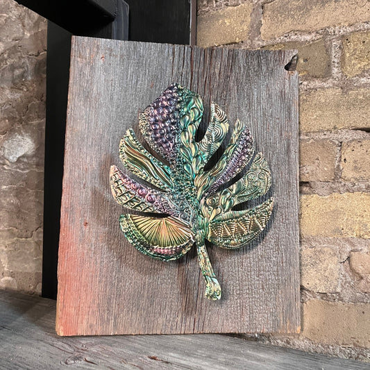 Decorative copper leaf sculpture on a wooden board against a stone wall background