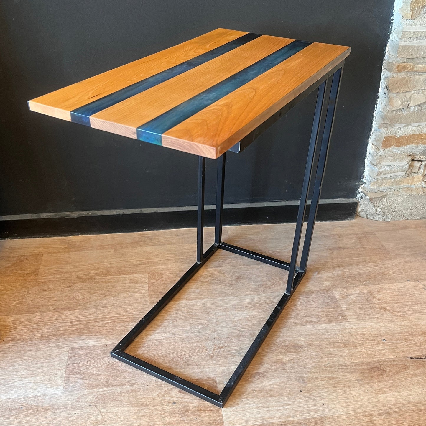 Wood and epoxy side table with black metal legs against a dark wall.