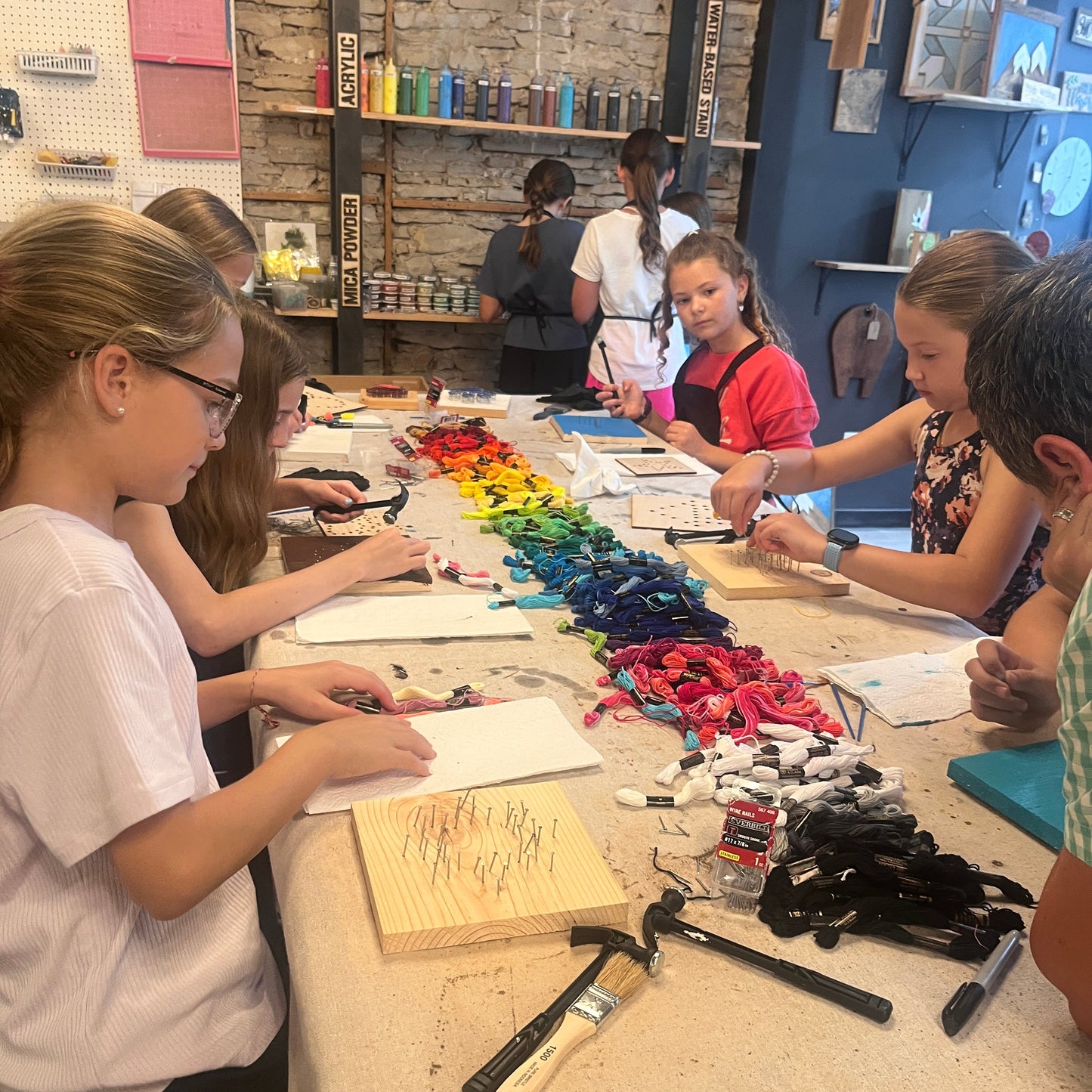 Children engaged in a string art craft activity at a table with various materials.