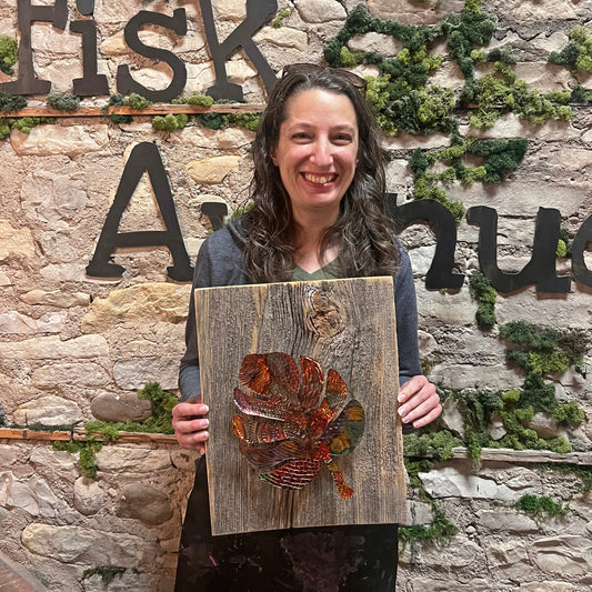 Person holding a wooden plaque with a copper leaf design in front of a stone wall with 'Fisk Avenue' sign.