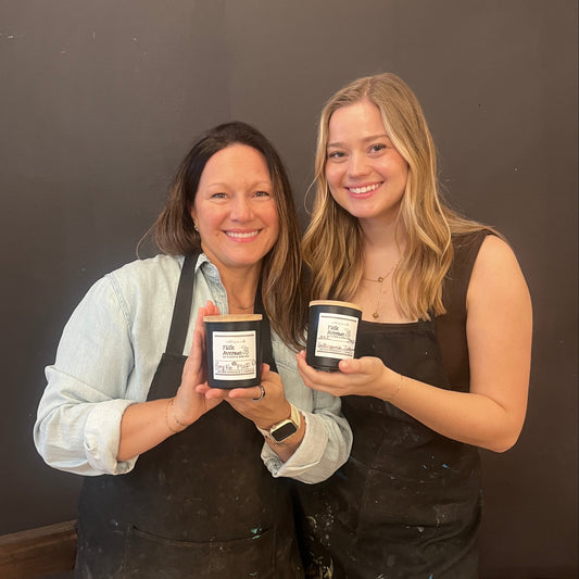 Two women holding handmade candles with handwritten labels against a dark background