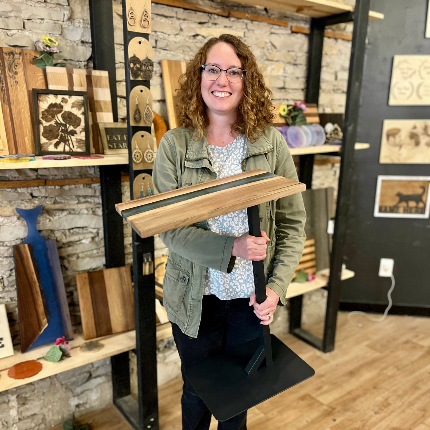 Woman holding a wooden epoxy river side table with live edge wood and a black metal base in a studio setting.