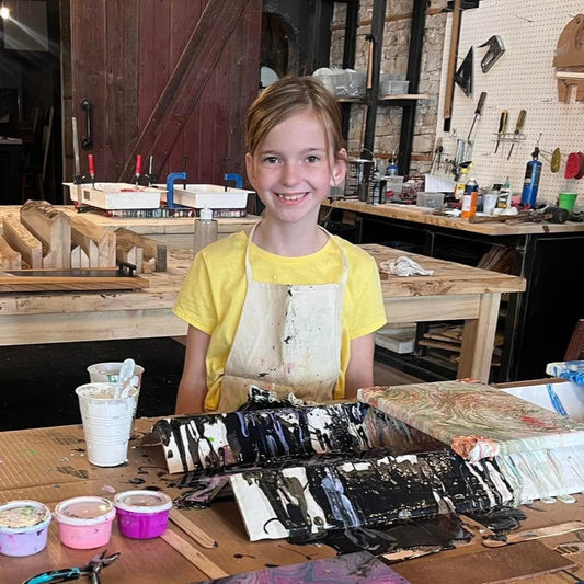 Young girl in a workshop with acrylic pour painting art supplies and canvases on a table