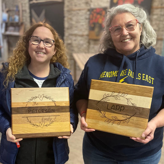 Two smiling individuals holding engraved wooden cutting boards.
