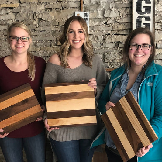 Three people smiling and holding freshly made striped solid wood cutting boards.