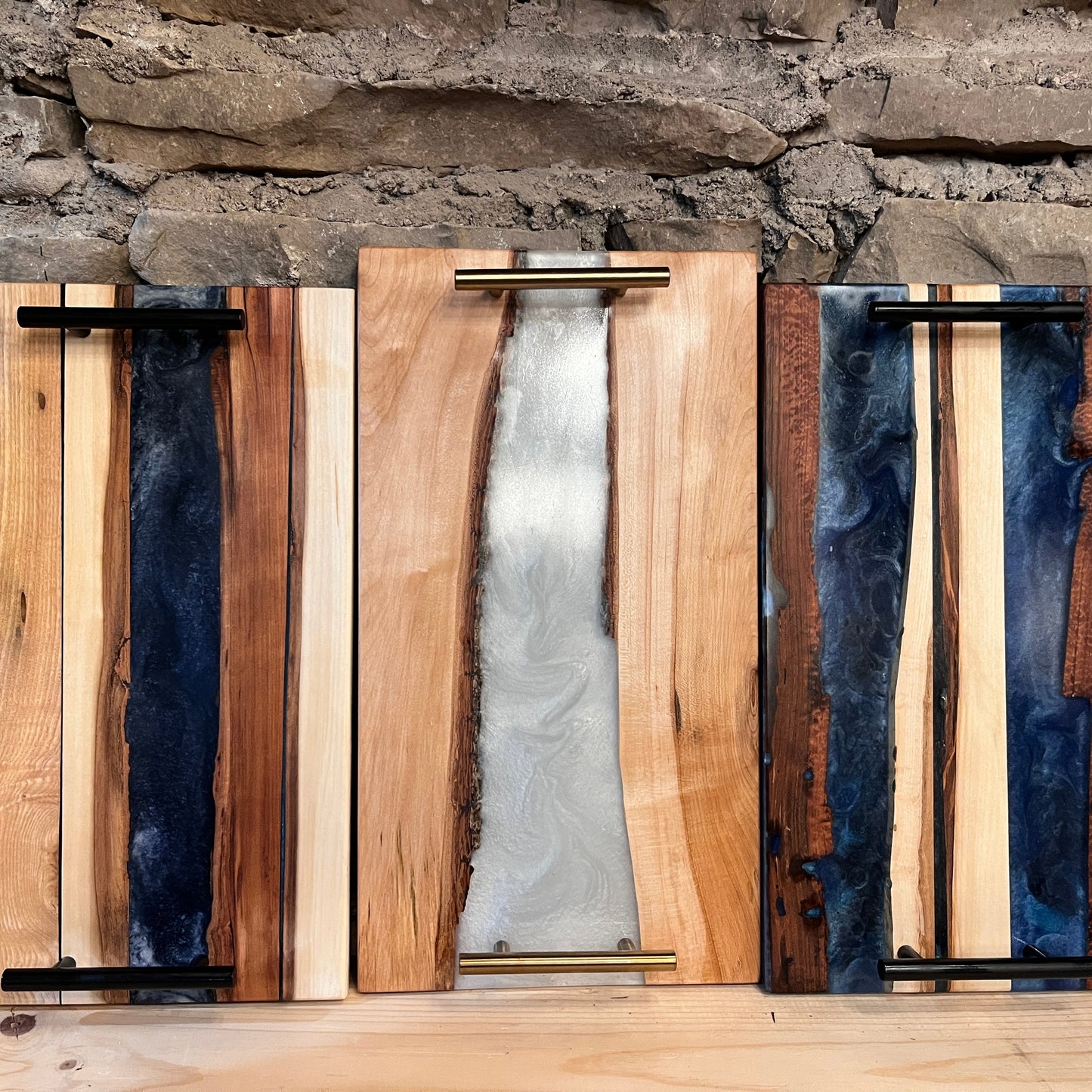 A display of three epoxy projects with wood, arranged on a table against a rustic backdrop.