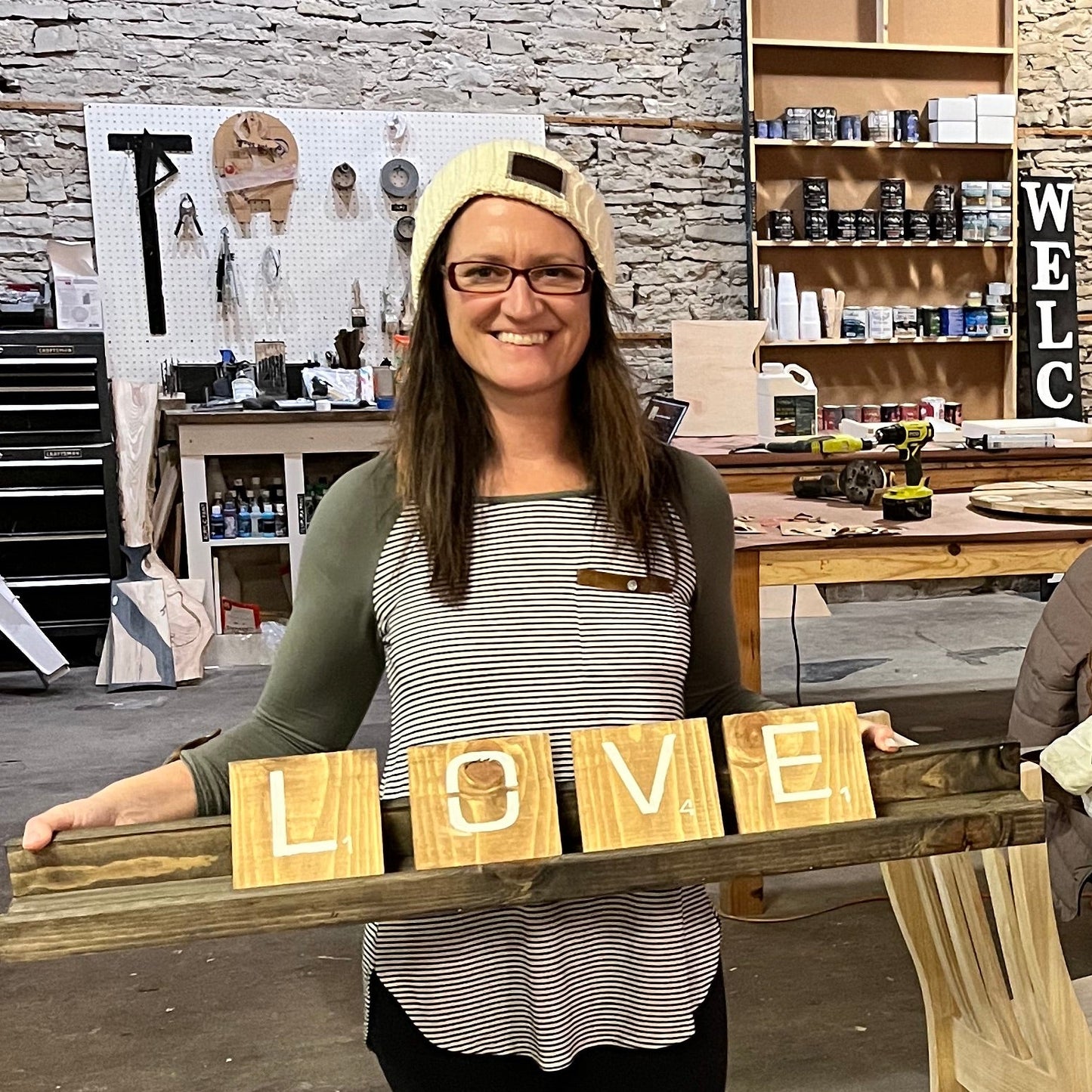 Person holding a wooden sign with letters spelling 'LOVE' in a workshop setting.