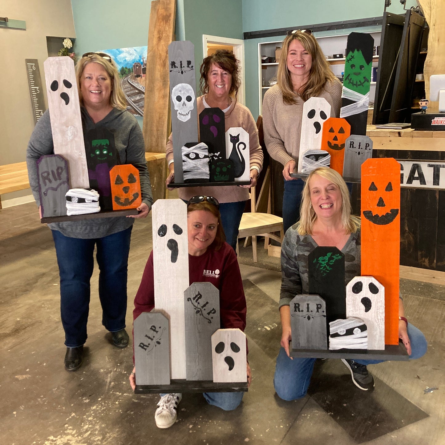 A group of people holding up their custom-painted Halloween front porch decorations, featuring various stencils such as ghosts, skulls, and pumpkins.