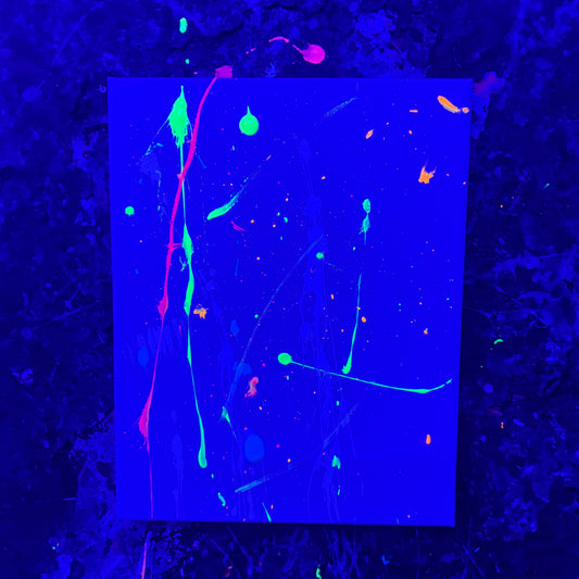 A canvas featuring neon splatters and drips in green, pink, orange, and blue in a splatter room with black lights.