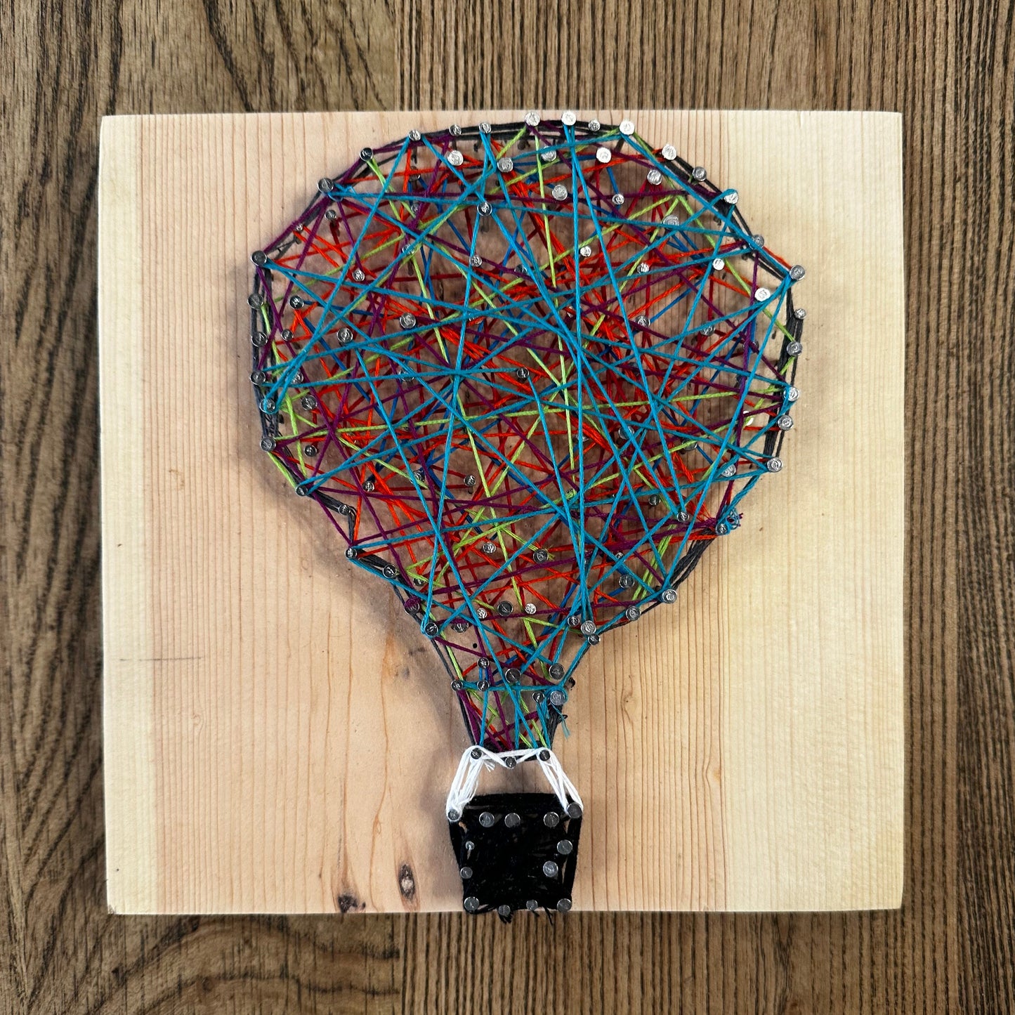 Wooden string art craft with a colorful hot air balloon design on a wood surface