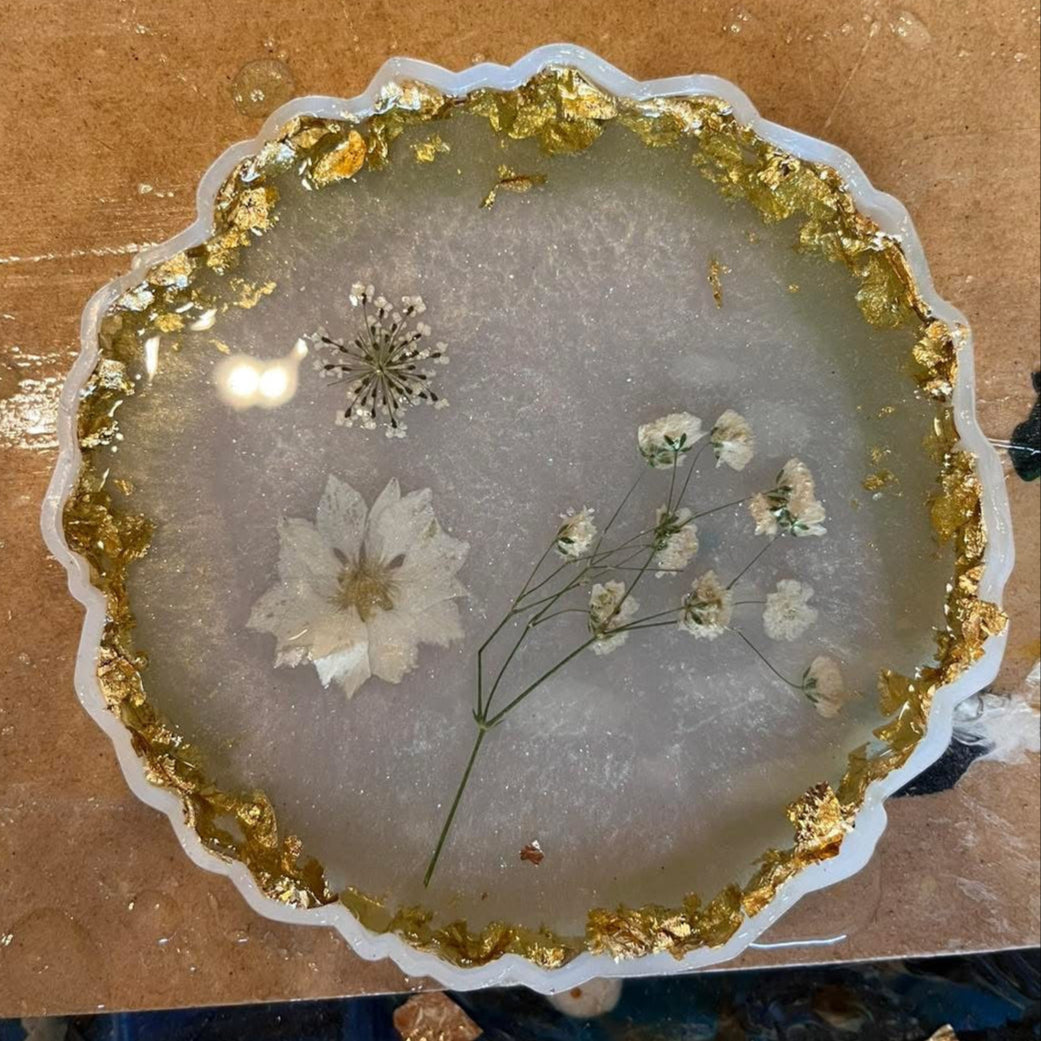Decorative epoxy coaster with gold leaf rim and pressed flowers in a pearl background