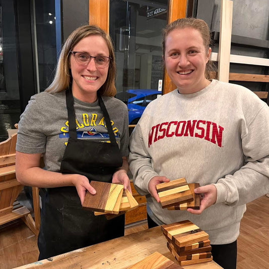 Two women holding wooden coasters in a workshop setting