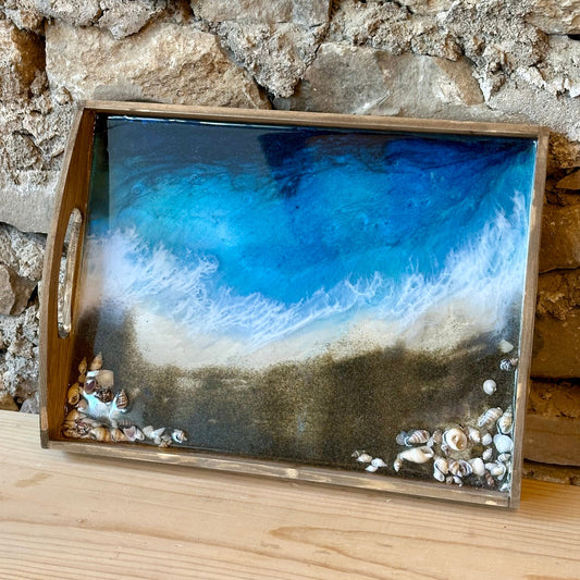 Decorative epoxy ocean pour tray with a beach scene design on a stone wall background