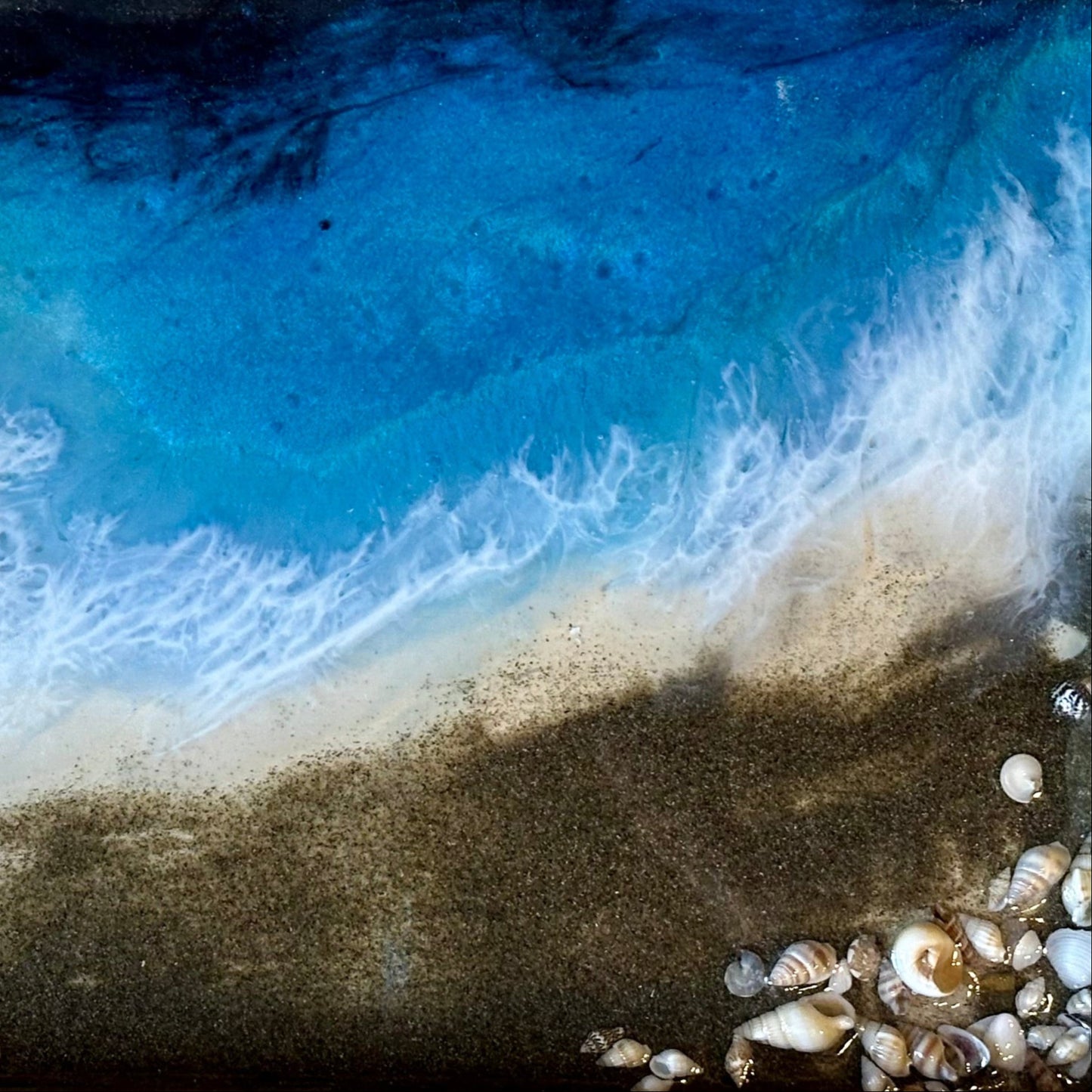 Close-up of an epoxy ocean pour tray with blue water, sand, and shells