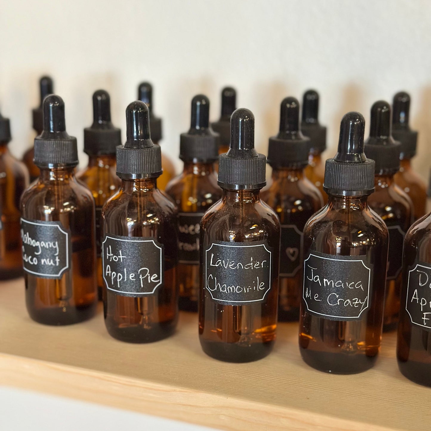 Row of brown glass bottles of essential oils with dropper caps on a wooden shelf.