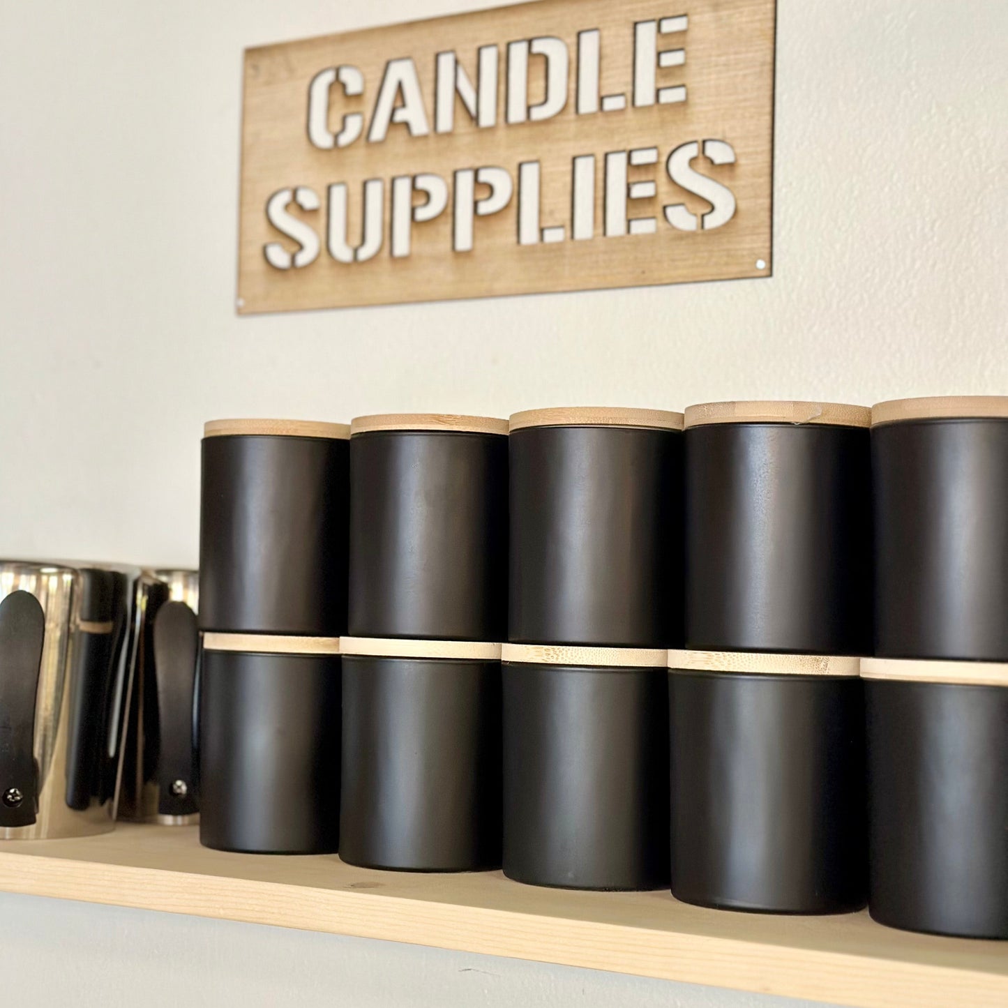 Black candle containers on a shelf with a 'Candle Supplies' sign above.