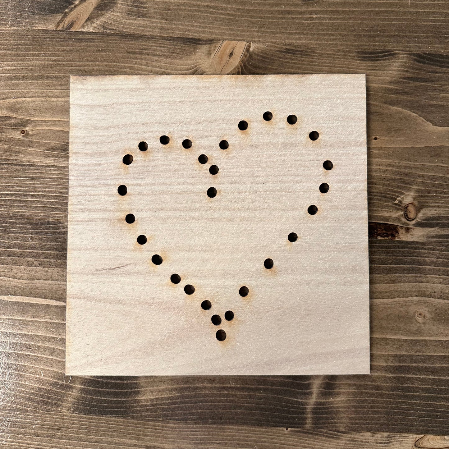 Wooden heart string art template design with drilled holes on a wooden background