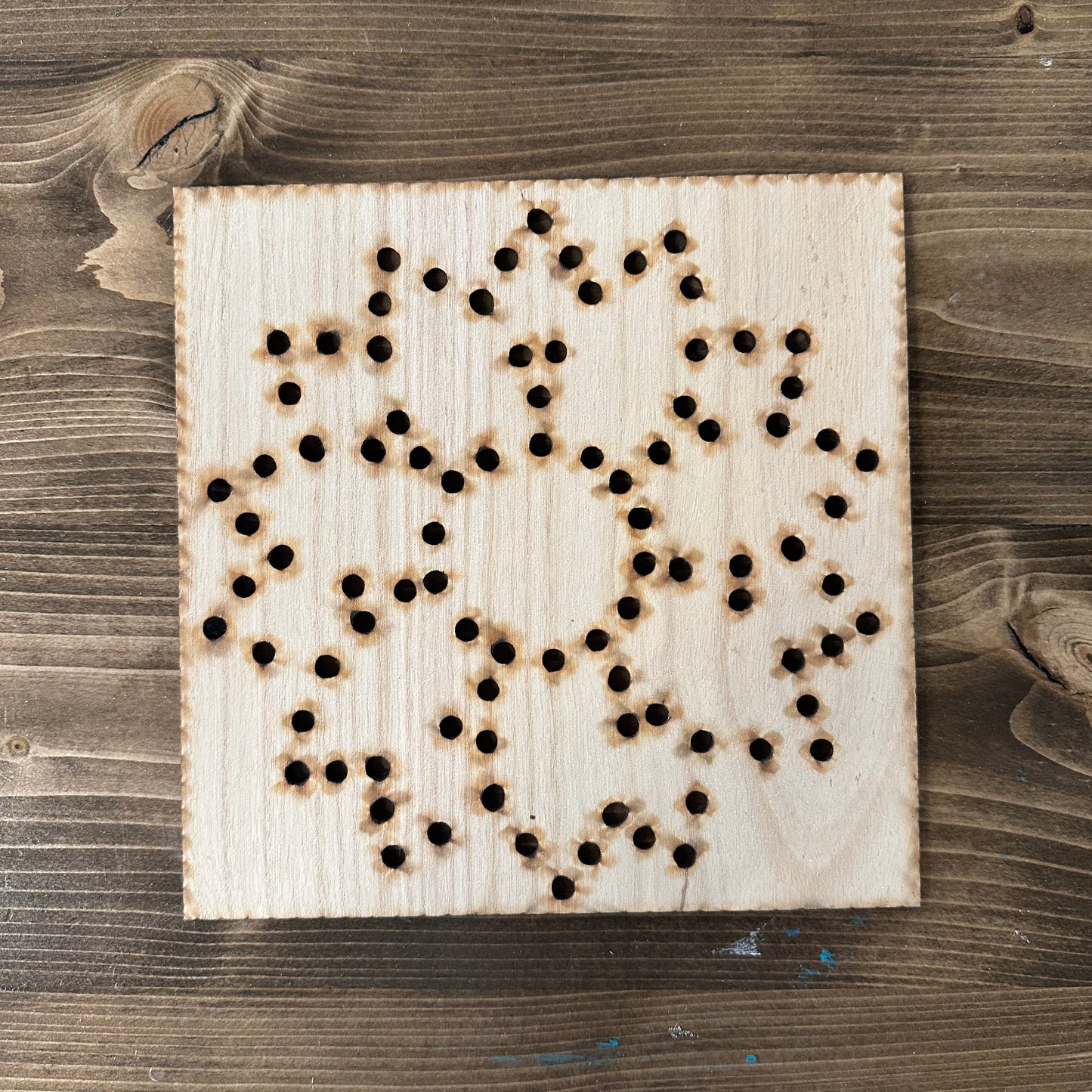 Wooden flower string art template design with drilled holes on a wooden background