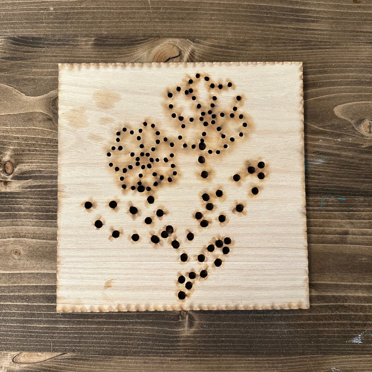 Wooden flower bouquet string art template design with drilled holes on a wooden background