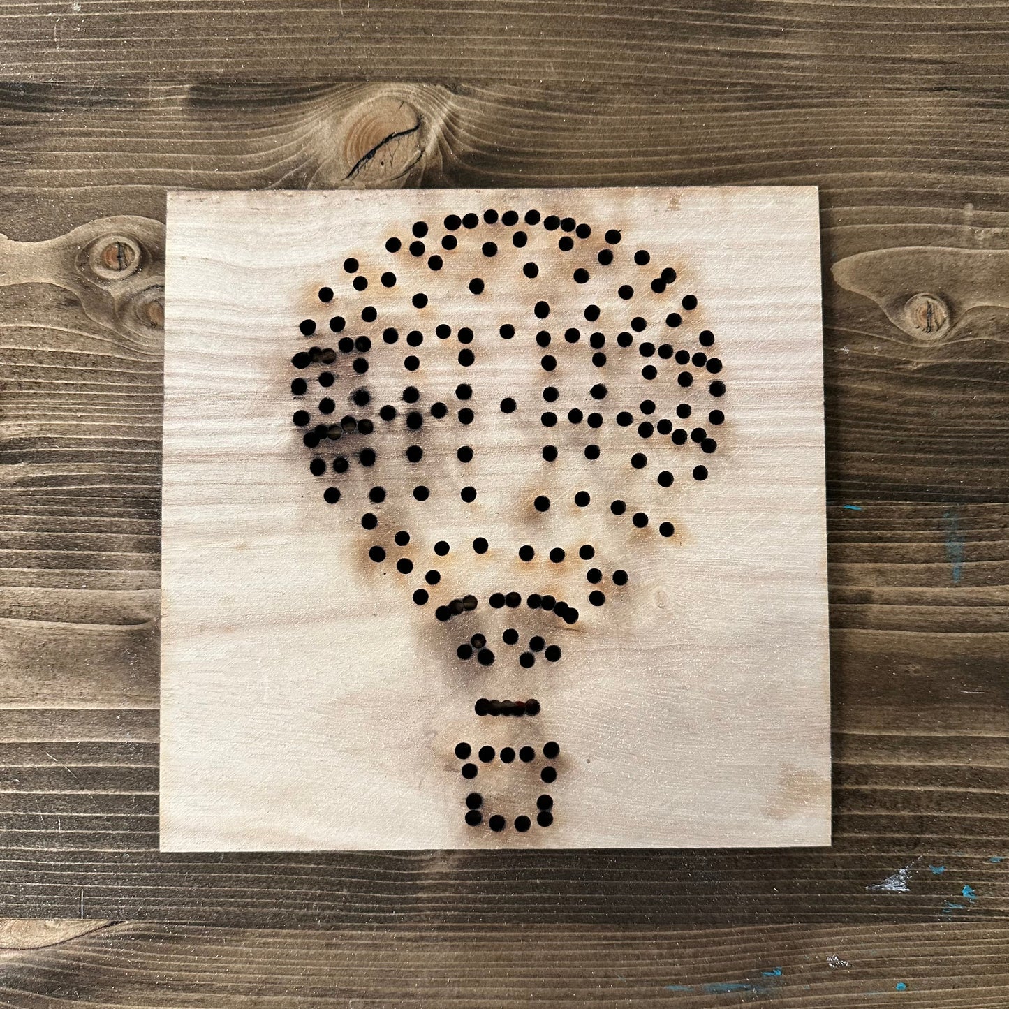 Wooden hot air balloon string art template design with drilled holes on a wooden background