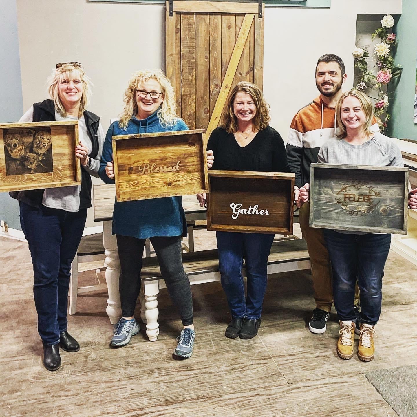 A group of four adults standing and holding up their handcrafted wooden trays with personalized engravings.