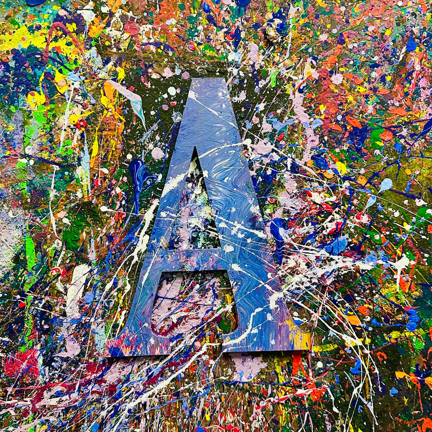 Wooden letter 'A' with splashes of color on a splatter painted wall.