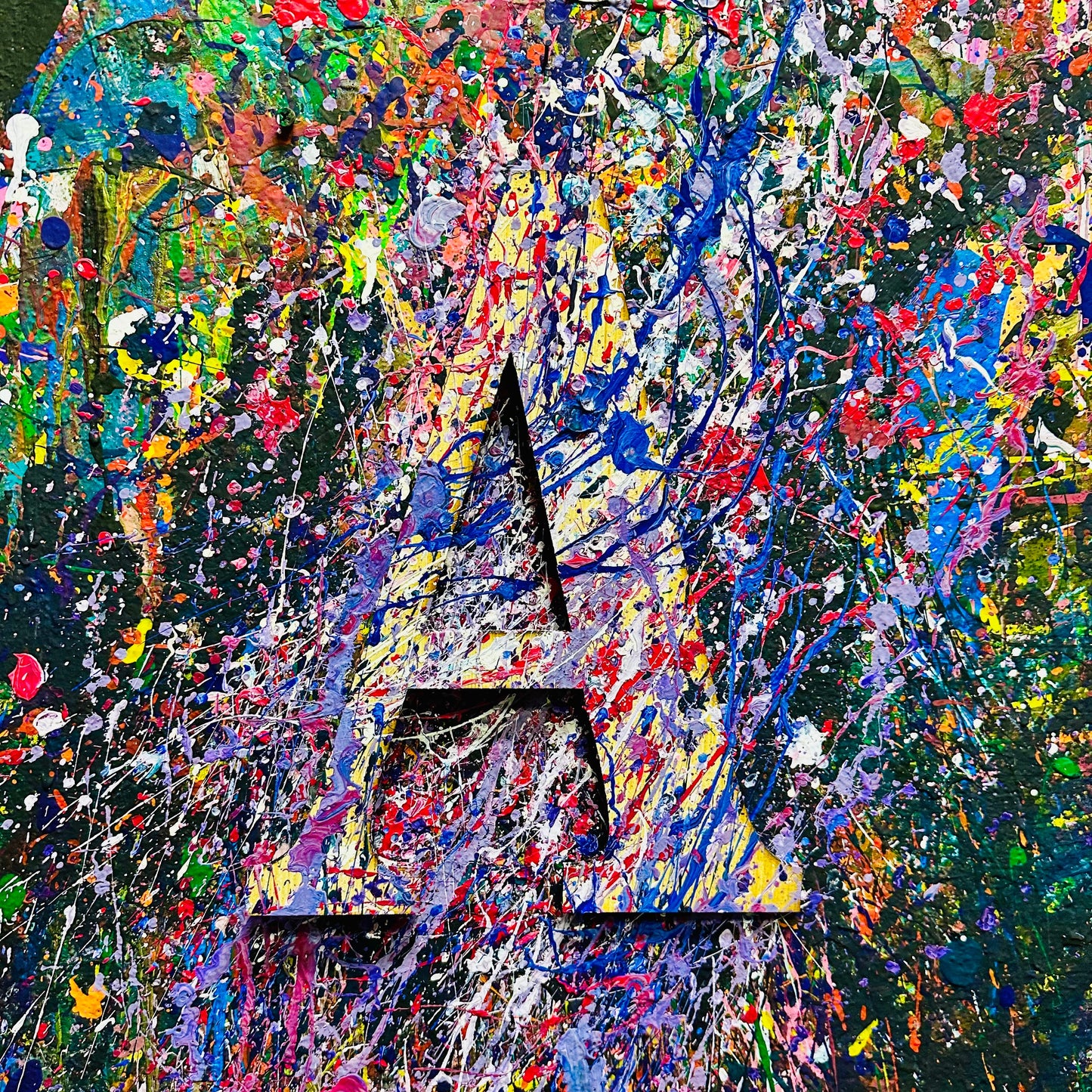 Wooden letter 'A' with splashes of color on a splatter painted wall.