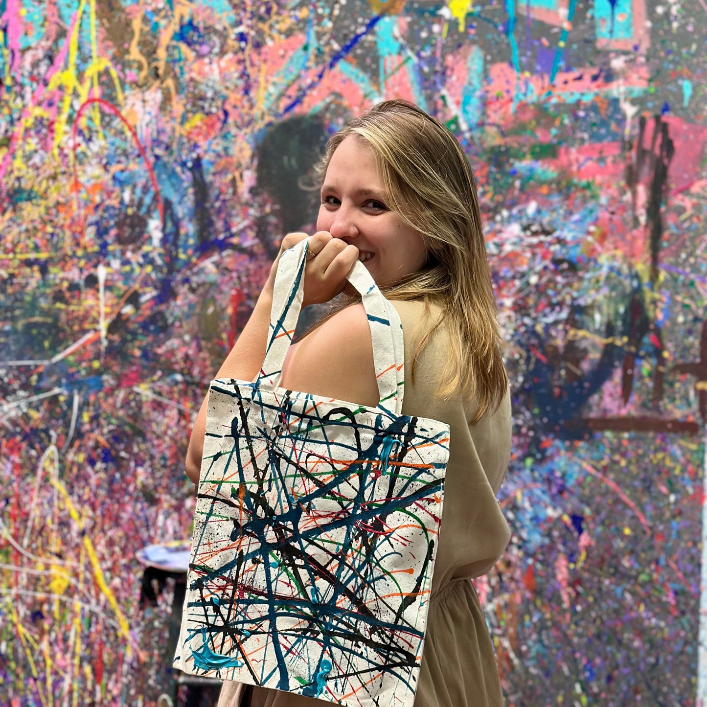 Woman holding a tote bag with abstract design in front of a colorful abstract painting.