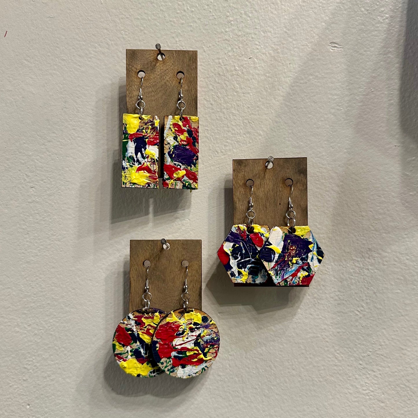 Colorful splatter painted earrings on wooden cards against a white wall
