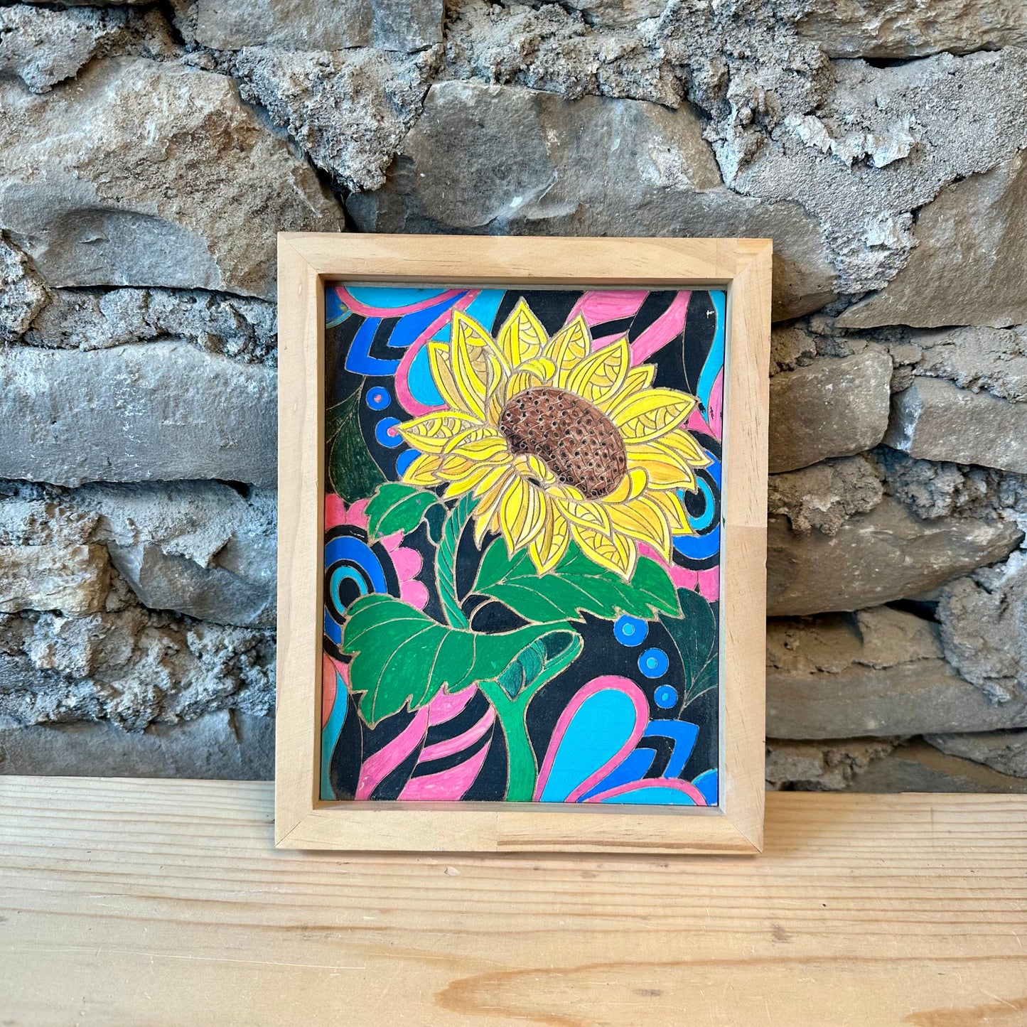 Framed colorful sunflower artwork against a stone wall.