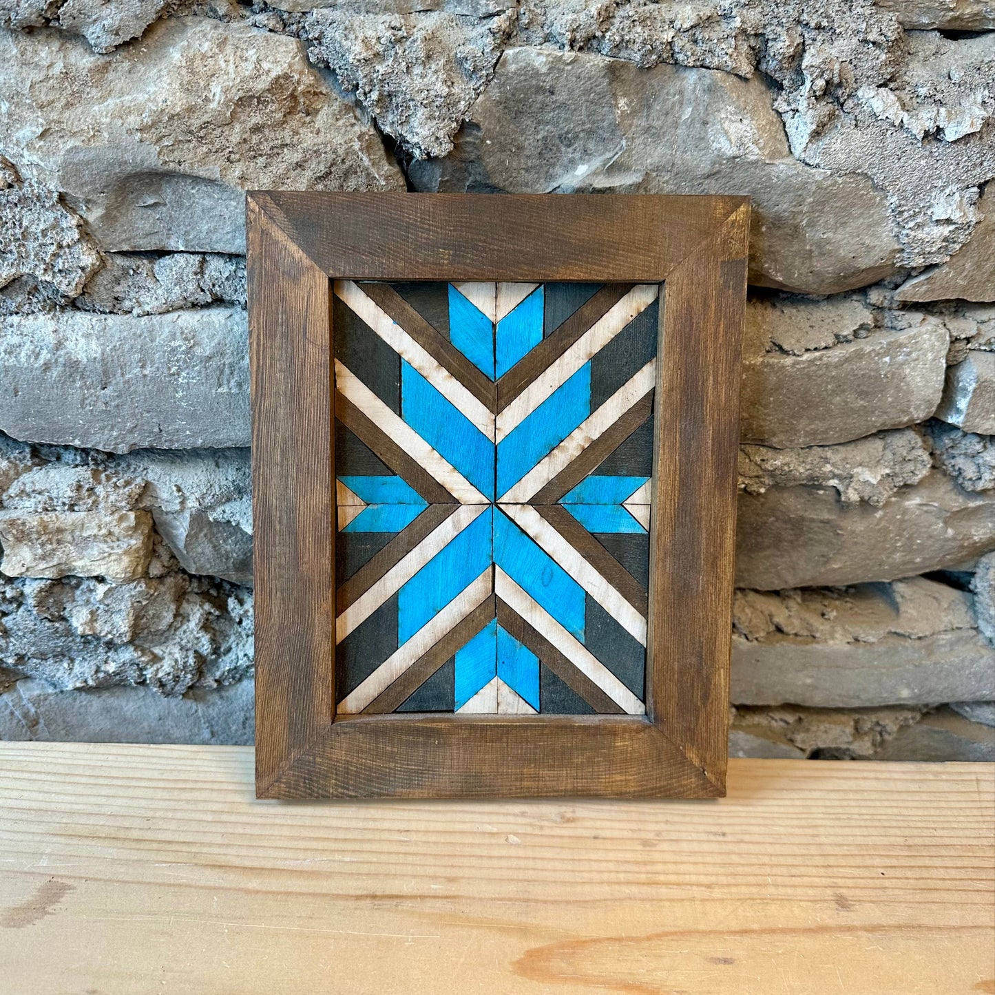 Decorative wooden frame with a geometric pattern against a stone wall.