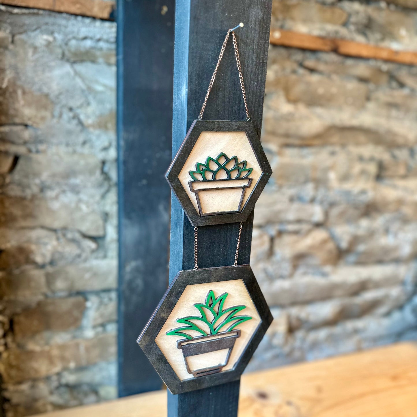 Decorative wall hanging with plant designs on a wooden surface against a stone wall.