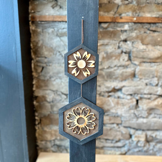 Decorative wooden art with floral designs on a wooden surface against a stone wall.