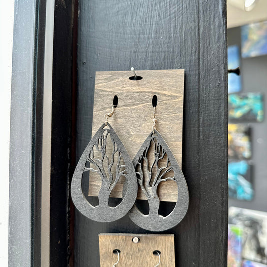 Wooden tree-shaped earrings on a display card against a dark background.