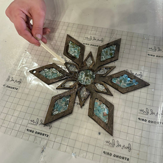 Decorative wooden snowflake suncatcher with epoxy and crystals on a grid surface