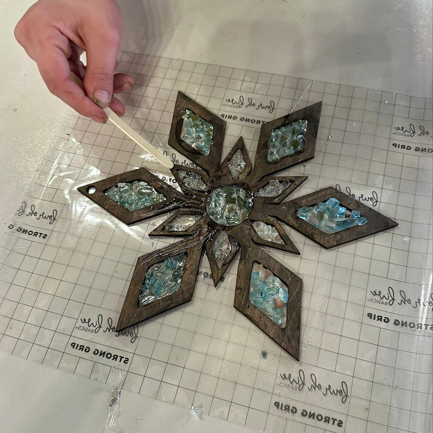 Decorative wooden snowflake suncatcher with epoxy and crystals on a grid surface