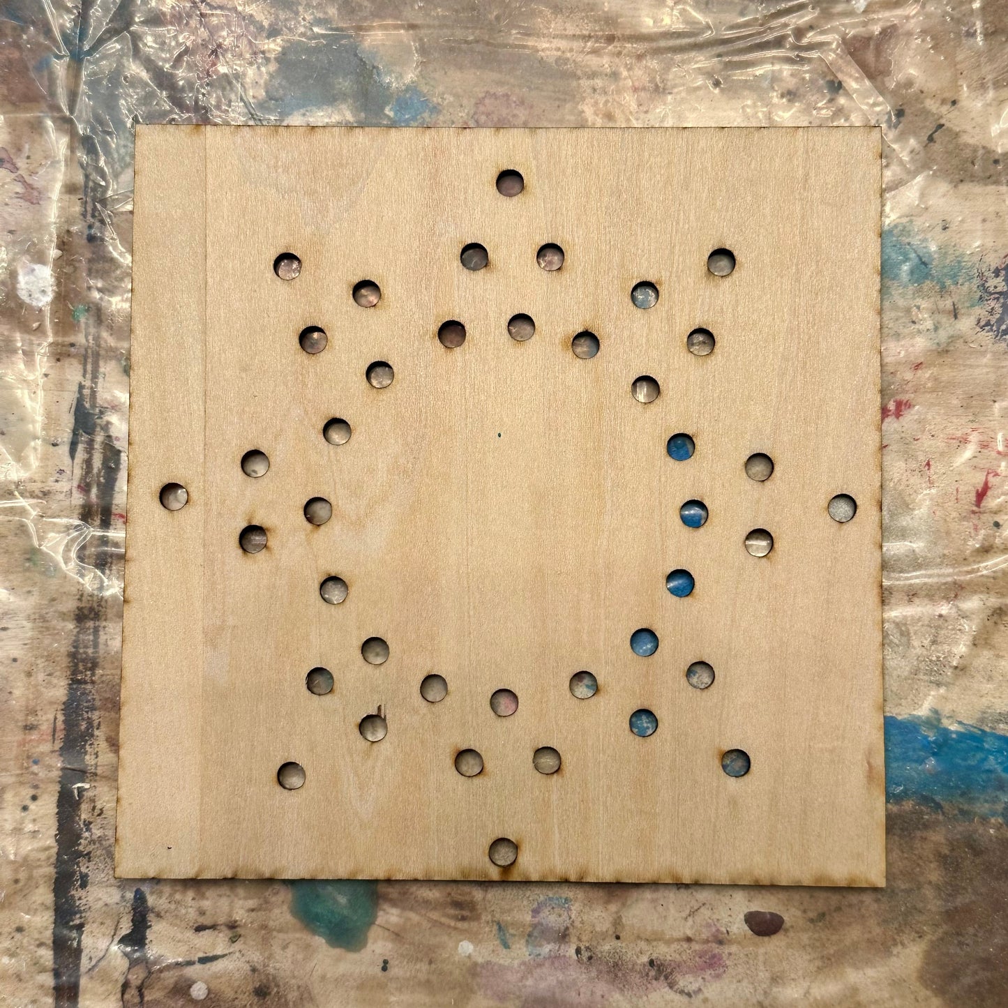 Wooden string art template with holes in a sun shape on a textured table background