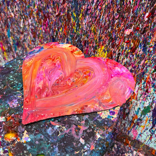 Heart-shaped wooden cutout with colorful paint splashes on a textured surface