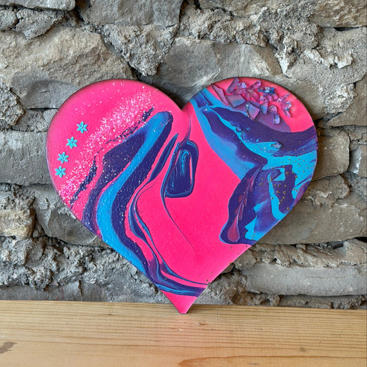 Pink and blue marbled wooden heart by a stone wall on a wooden shelf.