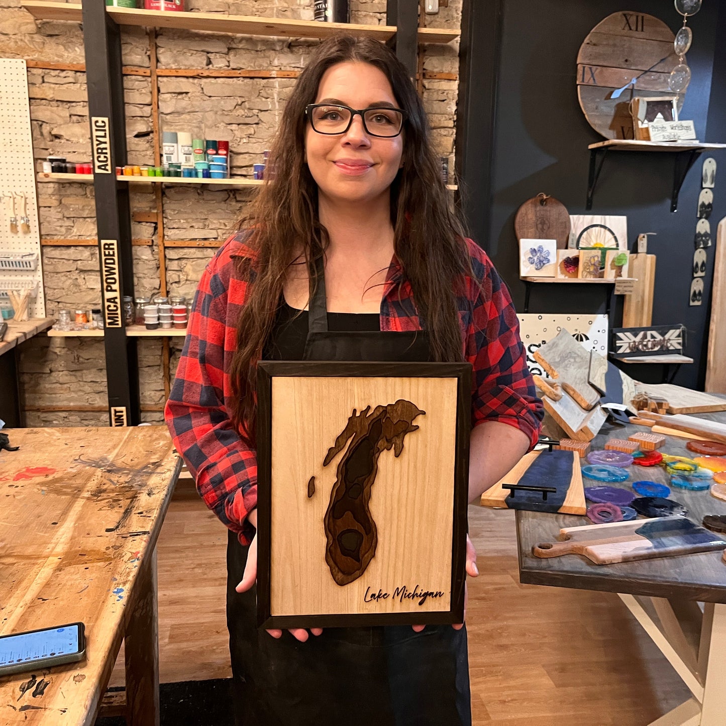 Woman holding a wooden plaque with a lake map design in a workshop setting