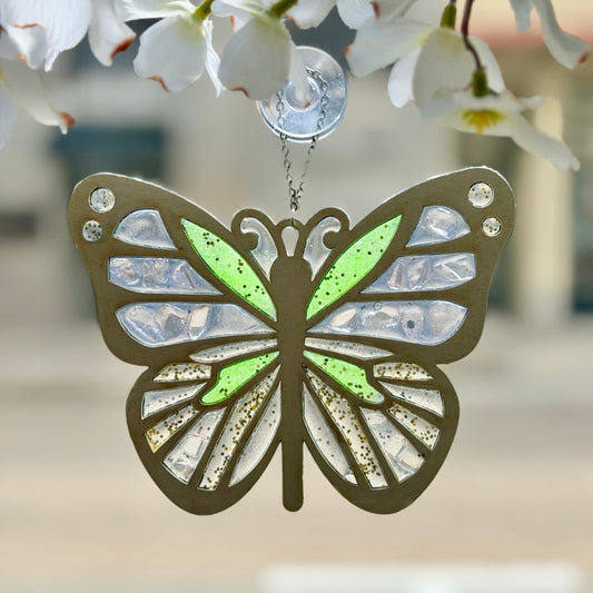 Butterfly-shaped suncatcher hanging against a blurred floral background.